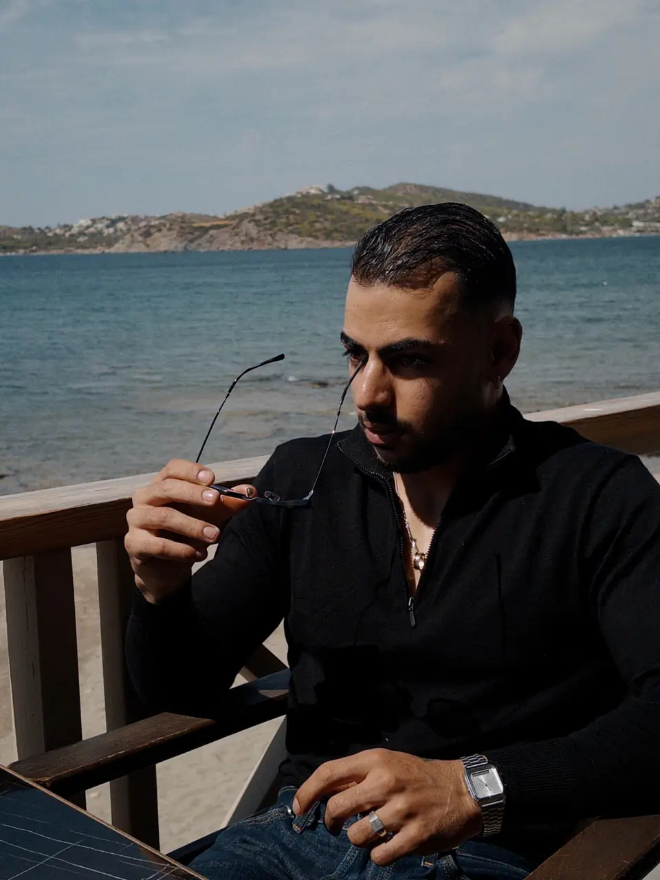 Roei Shirav, founder of Shirav Labs, seated by the sea in Greece, sunglasses in hand.